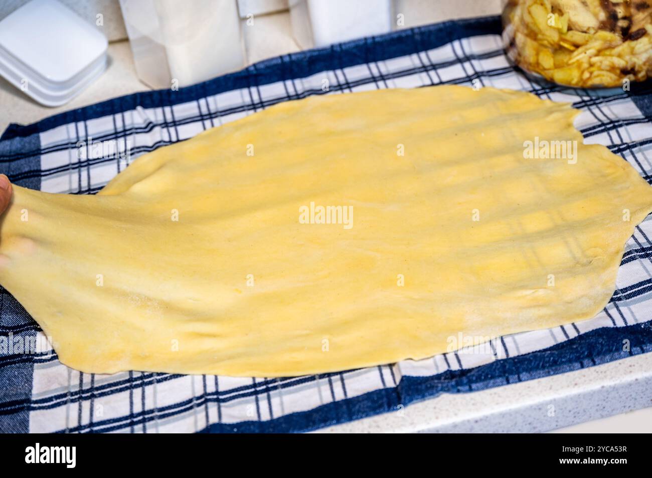 Pulling homemade dough for strudel on checkered towel, closeup. Stock Photo