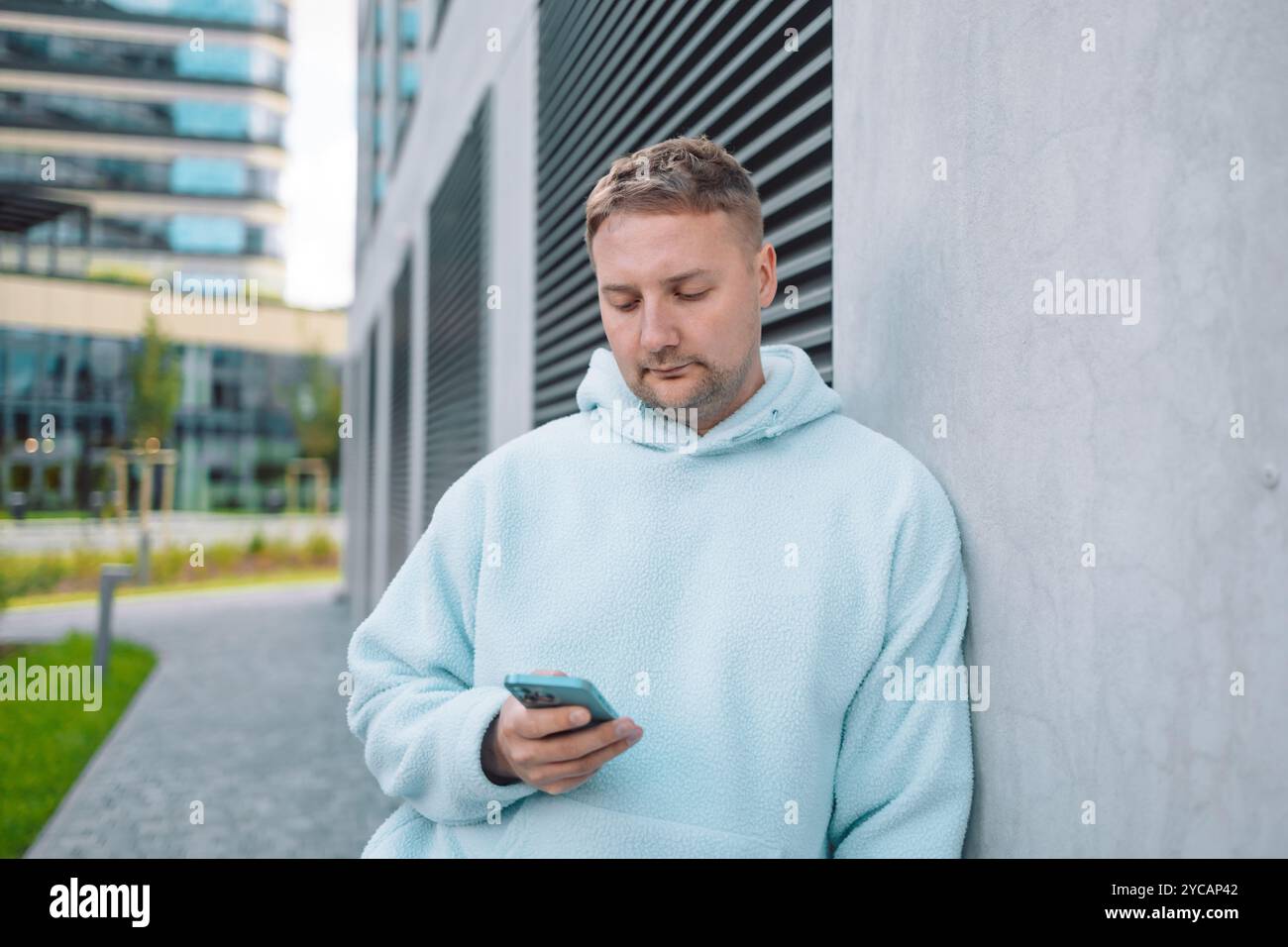 Successful young Caucasian man walking outside office building, engineer software developer programmer smiling and happy using test app on phone Stock Photo