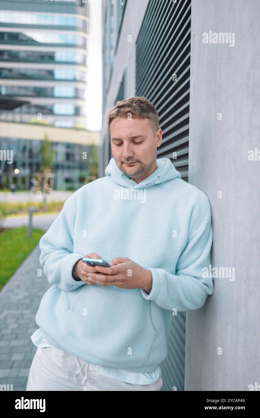 Successful young Caucasian man walking outside office building, engineer software developer programmer smiling and happy using test app on phone Stock Photo
