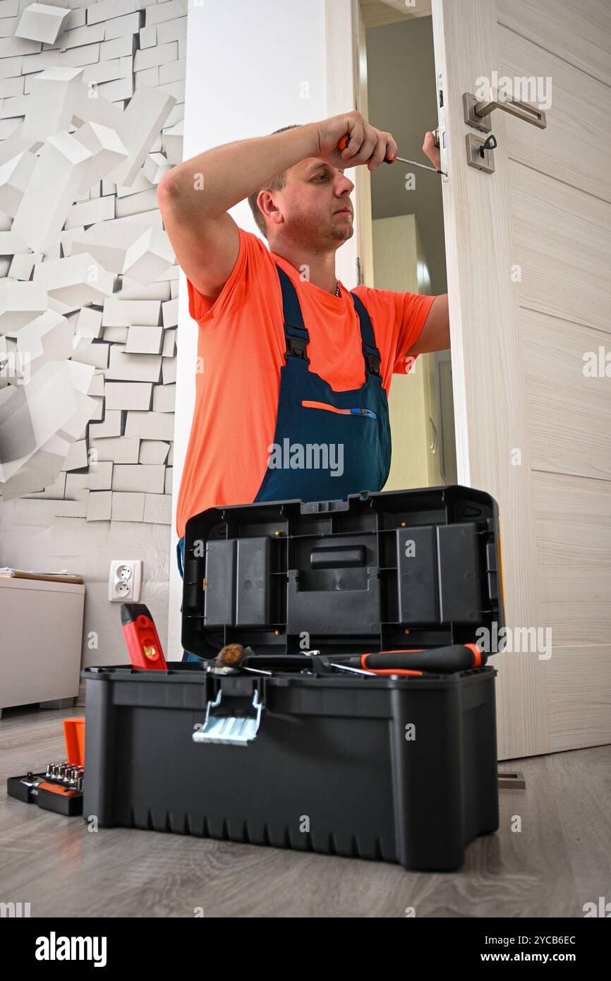 Handyman is standing with his toolbox open and using a screwdriver to ...