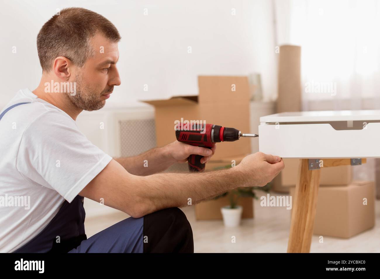 Side-View Of Carpenter Man Assembling Table Using Electric Drill Indoors Stock Photo