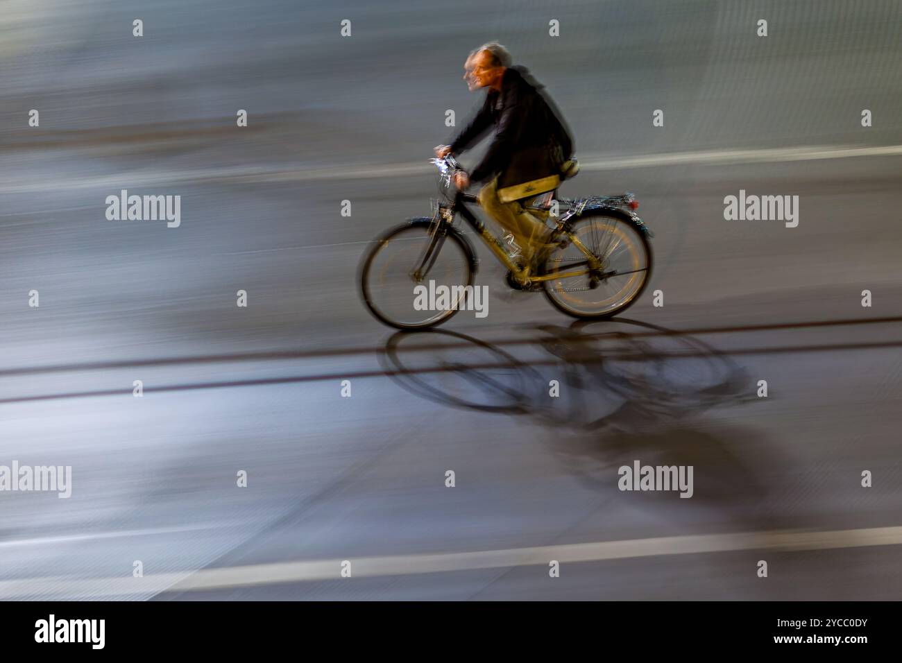 A man riding a bicycle on city streets at night, captured with a motion ...