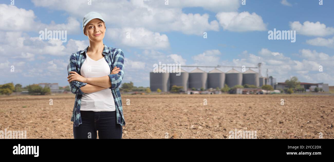 Female farmer posing with crossed arms on a field with silos towers ...