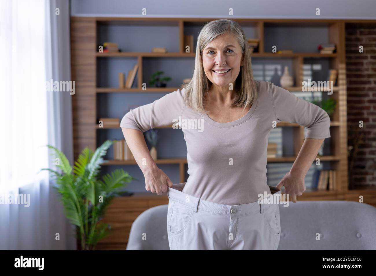 Joyful Mature Woman Stands Confidently Showing Weight Loss Wearing joyful-mature-woman-stands-confidently-showing-weight-loss-wearing