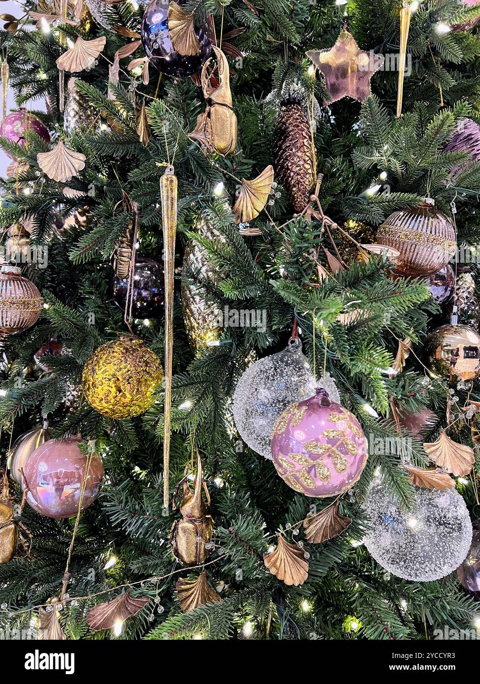 A close-up of shimmering Christmas ornaments hanging on a lush green tree - Smartphone Captured Stock Image