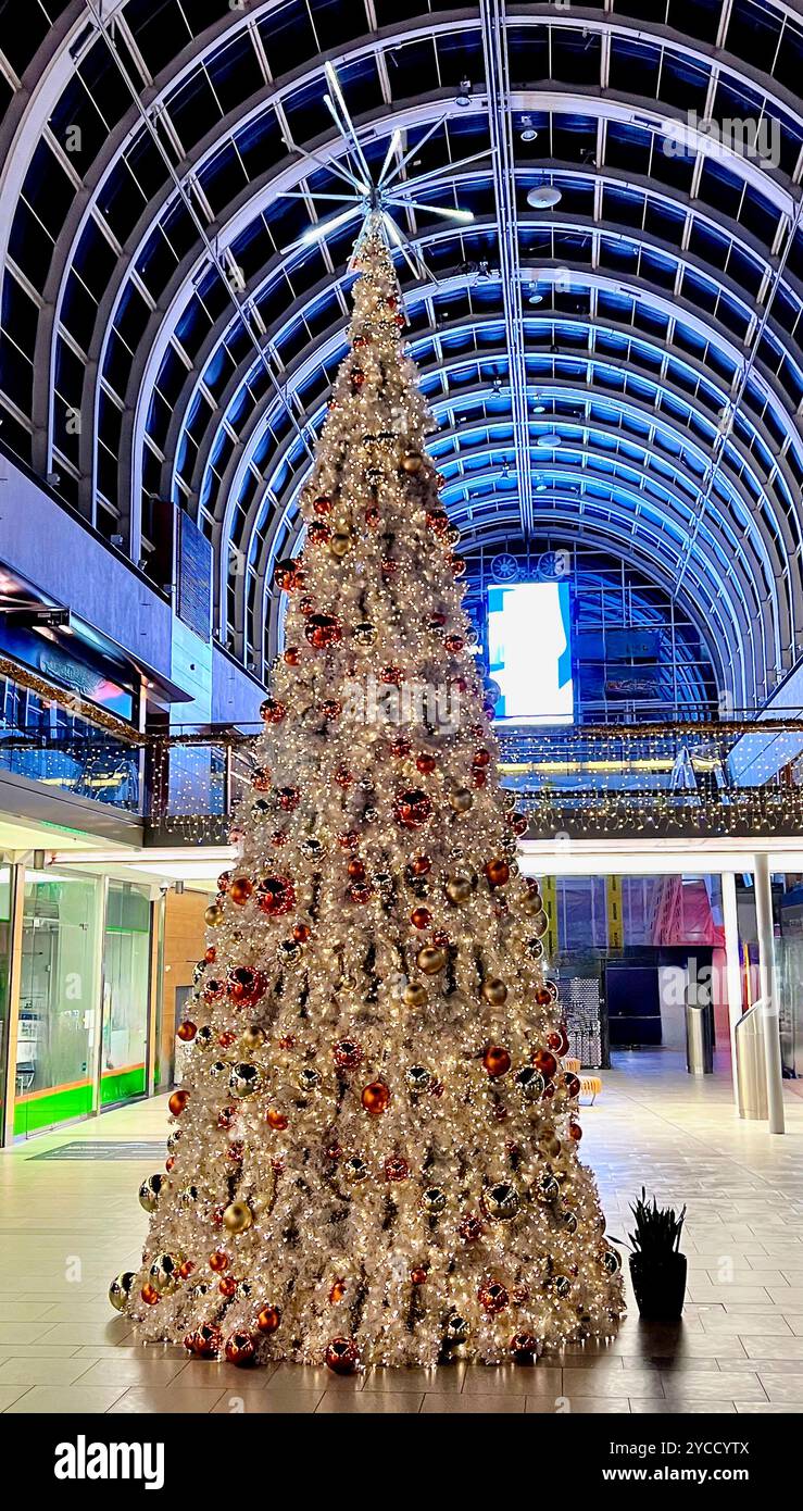 A grand Christmas tree stands at the center of a modern shopping mall, glowing with festive lights - Smartphone Captured Stock Image