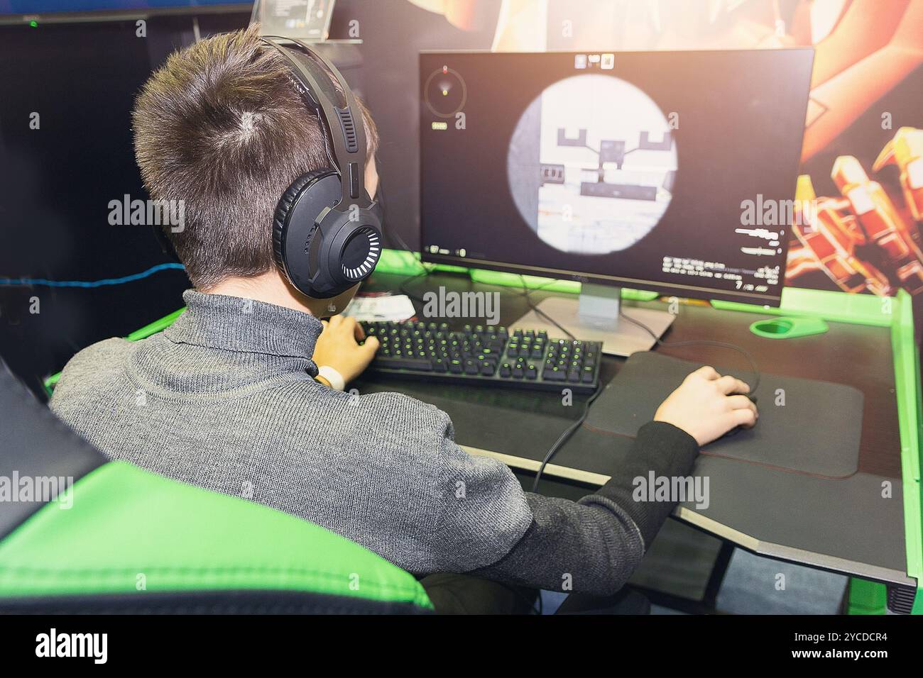A gamer is sitting in front of a large monitor with headphones, he is ...