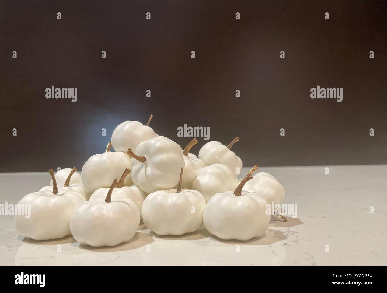 Pristine white mini pumpkins huddle together on marble, their stems casting delicate shadows under moody lighting, creating an ethereal autumn display. - Smartphone Captured Stock Image
