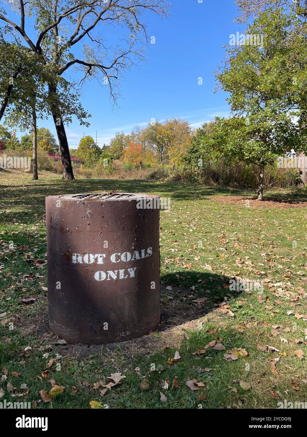 Metal barrel labeled 'HOT COALS ONLY' placed in a public park for safe disposal of grill embers. Captures outdoor safety, signage, and park life. - Smartphone Captured Stock Image
