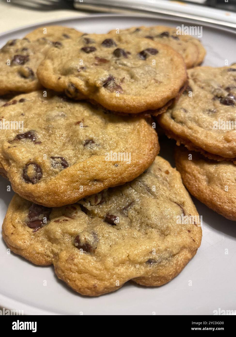 Warm, golden-hued chocolate chip cookies stack casually, their crisp edges and melty morsels catching the light in a cozy, homestyle scene. - Smartphone Captured Stock Image