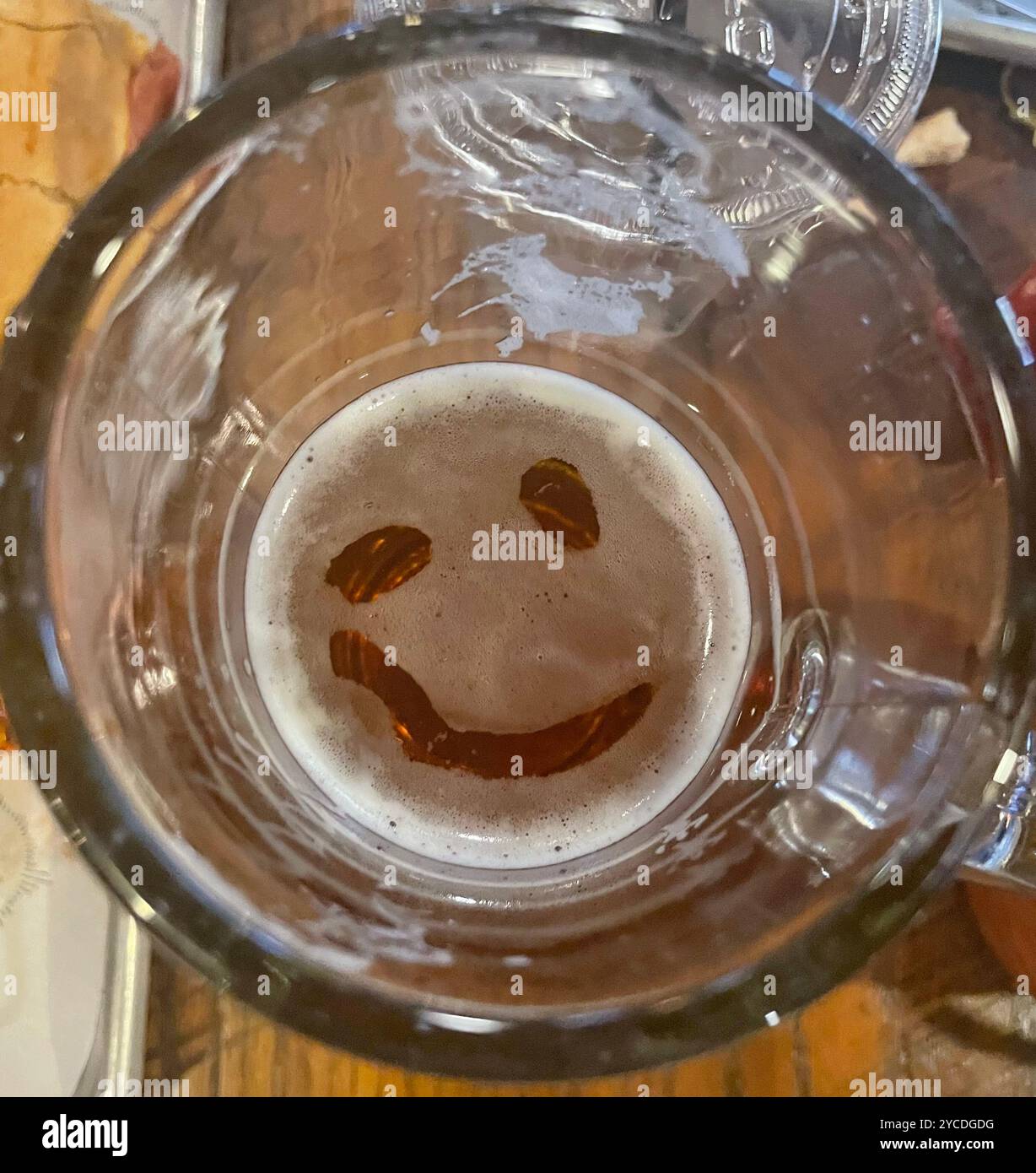 A playful smiley face emerges in the remaining beer foam at the bottom of a glass, creating an unexpected moment of cheer. - Smartphone Captured Stock Image