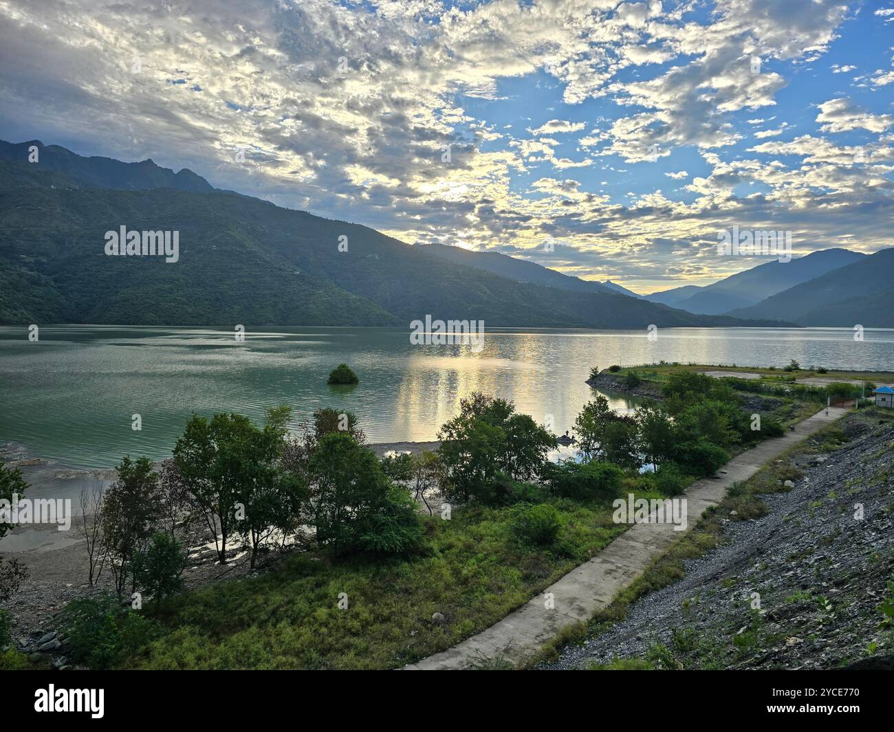 Serene lake at sunset with mountain reflections and a winding path. - Smartphone Captured Stock Image