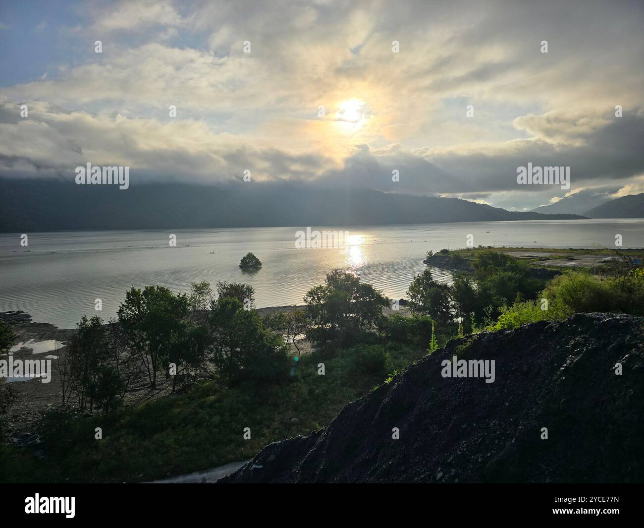 Tranquil moments by the lake as the sun breaks through the clouds, casting a golden glow on the calm waters. - Smartphone Captured Stock Image