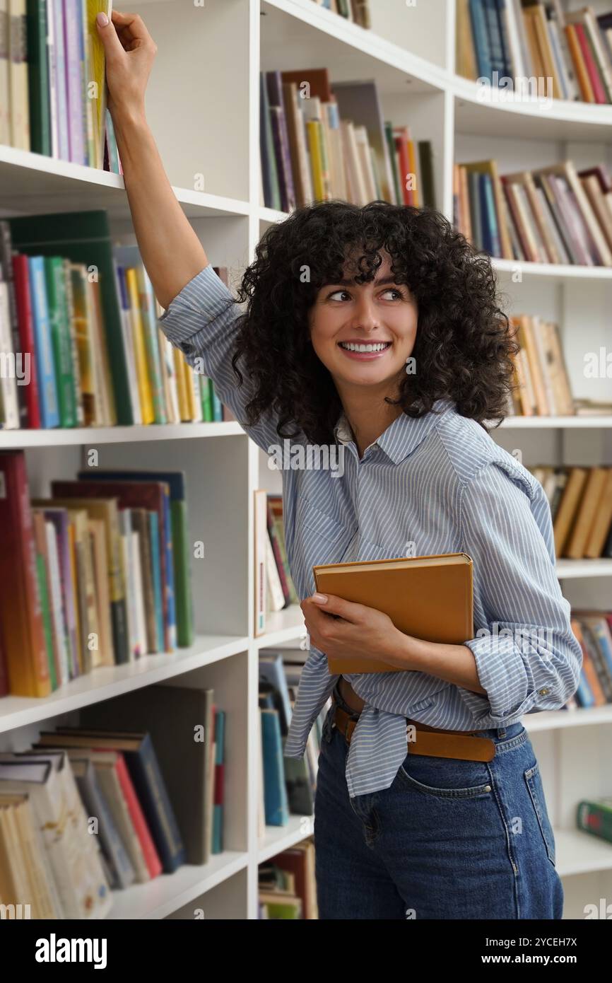 Cute smiling young curly-haired girl at the bookshelves Stock Photo - Alamy