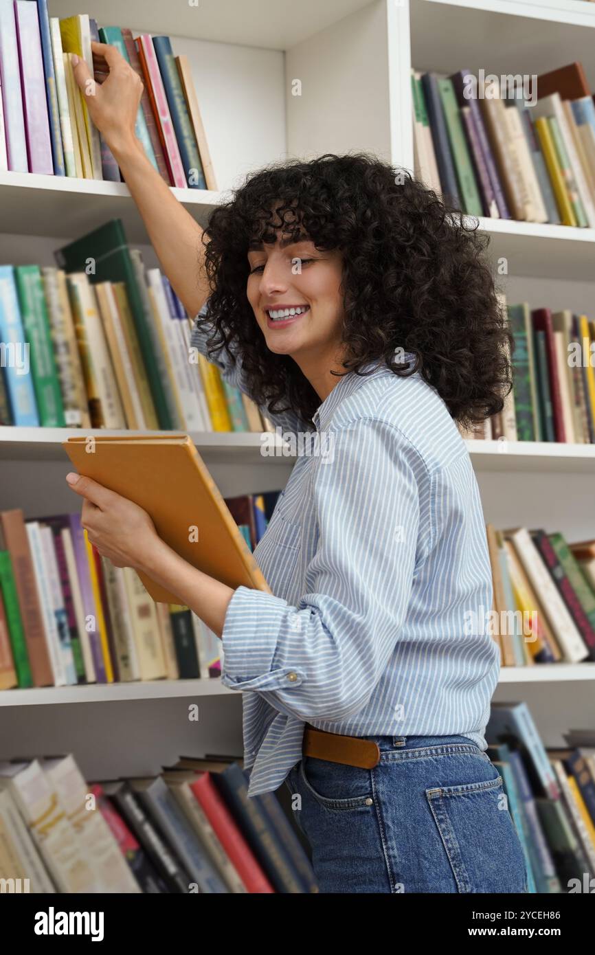 Cute smiling young curly-haired girl at the bookshelves Stock Photo - Alamy