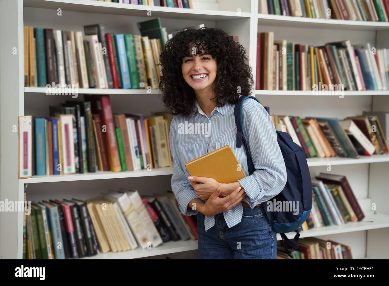 Sweet curly-haired young girl at the bookshelves in the library Stock ...