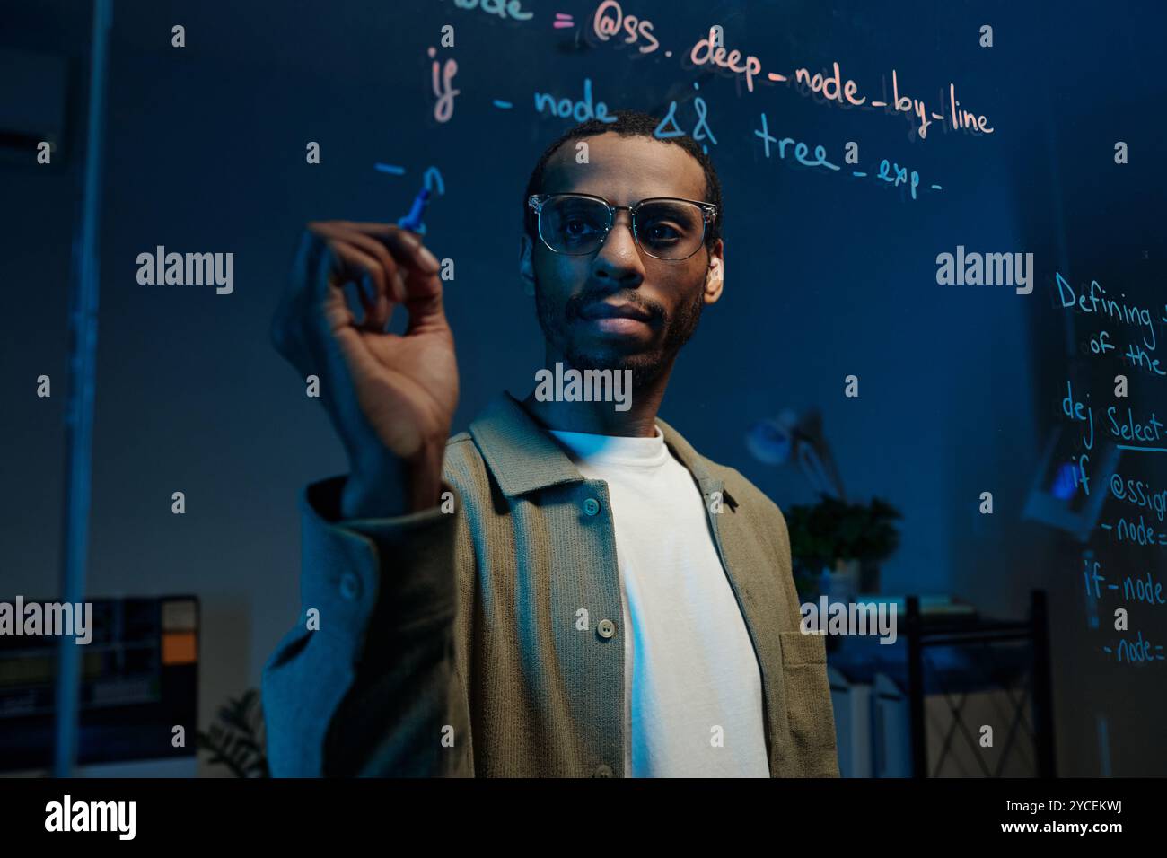 Man Writing Code on Transparent Board in Dimly Lit Room Stock Photo