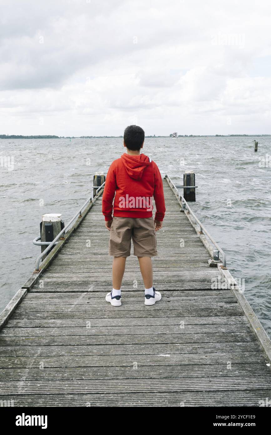 Back view of boy with casual clothing on wooden pier a cloudy summer day. Concept freedom Stock Photo