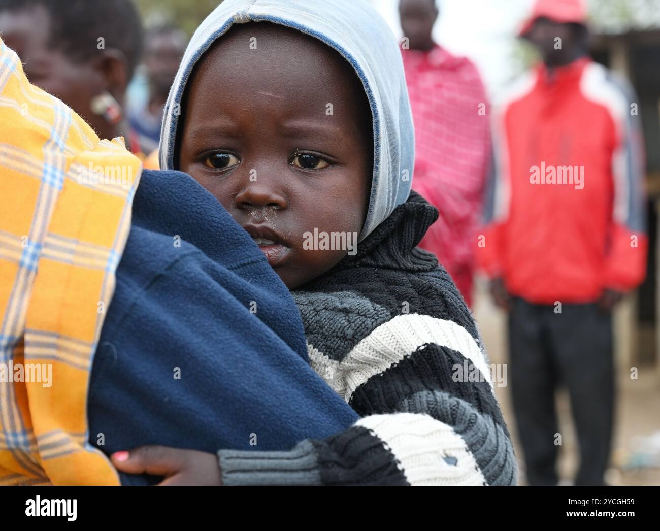 VILLAGE NEAR NAIROBI, KENYA - NOVEMBER 14, 2022:  Portrait of an African little girl from Masai tribe sitting behind his mother, Kenya, Africa Stock Photo