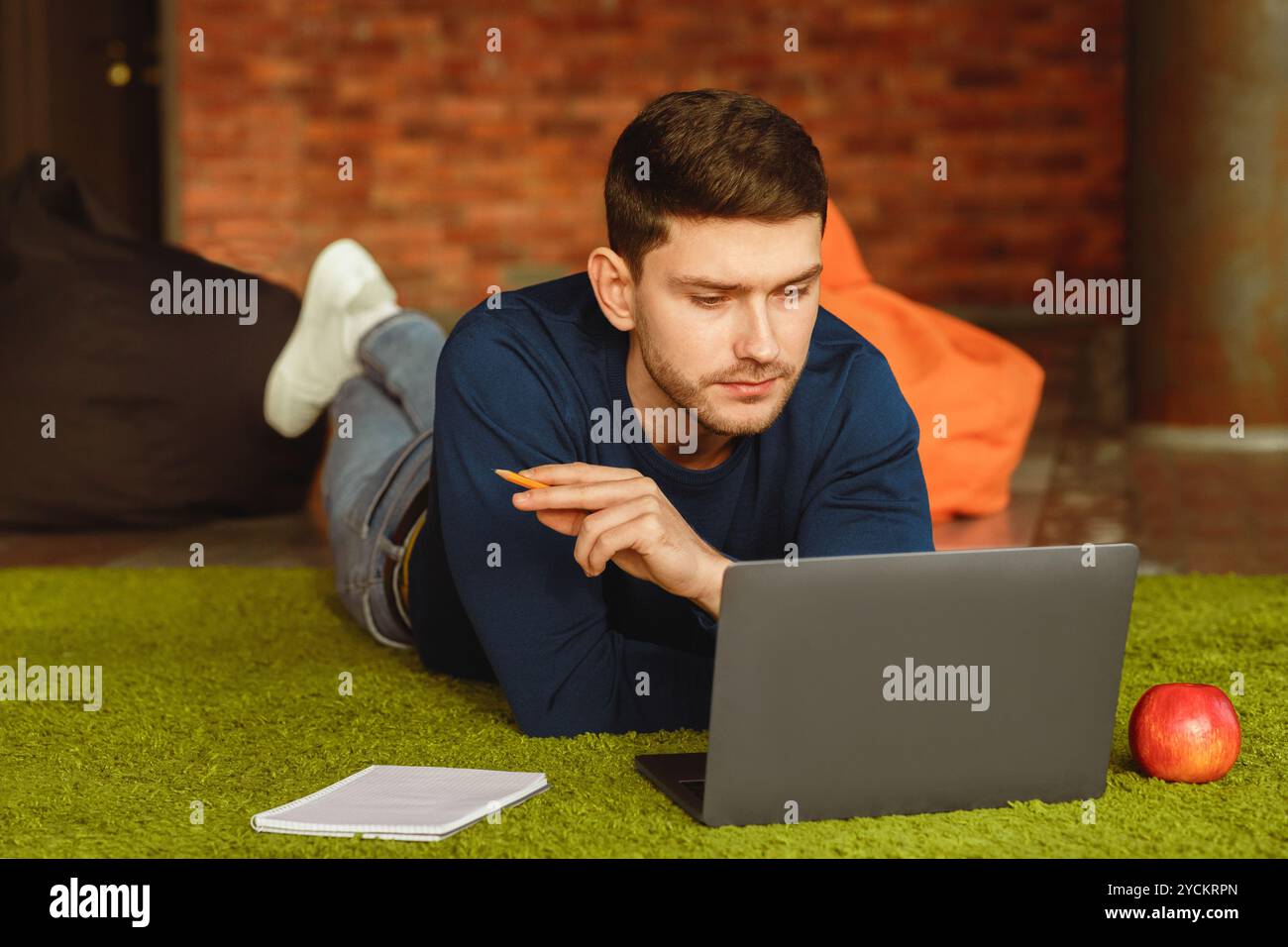 Millennial Guy Using Laptop Lying On Floor At Home Stock Photo