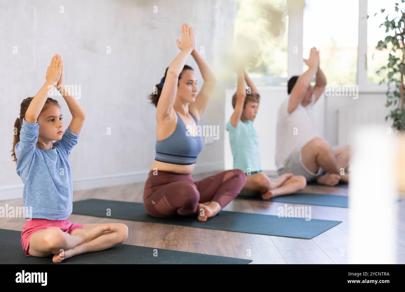 Mom with her family practices yoga in lotus position Stock Photo - Alamy