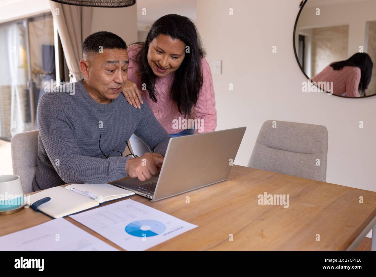 Multiracial senior couple using laptop at home, discussing finances with documents on table Stock Photo