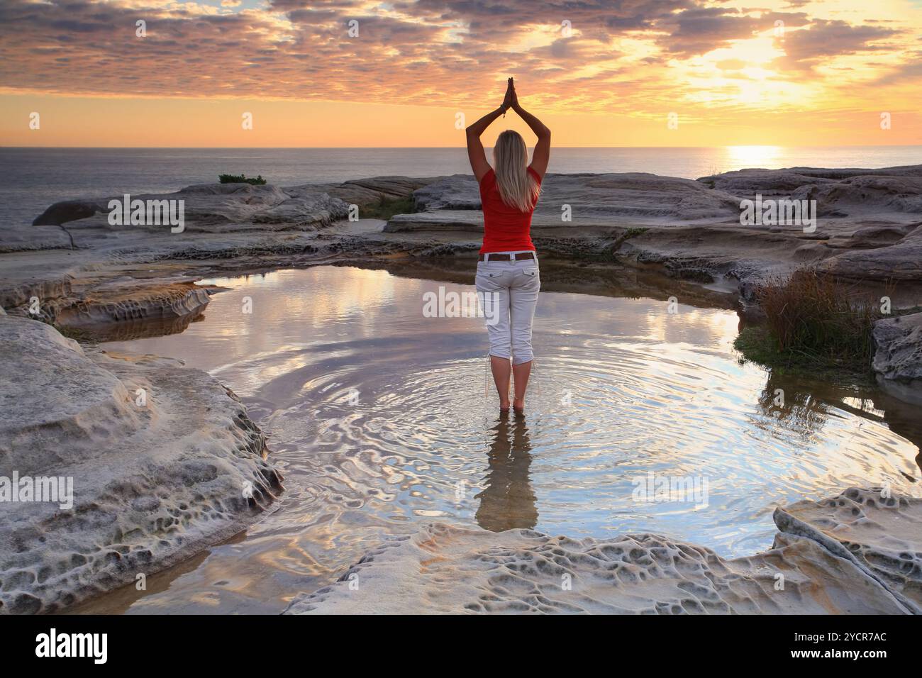 A woman standing by the ocean at sunrise, practicing yoga, meditation, pose.  Rejuvenating the soul, quiet time and solitude in natures beautiful surr Stock Photo