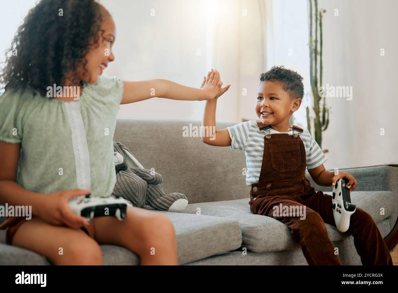 Kid Using Controller High five, controllers and children on sofa with video game for bonding ...