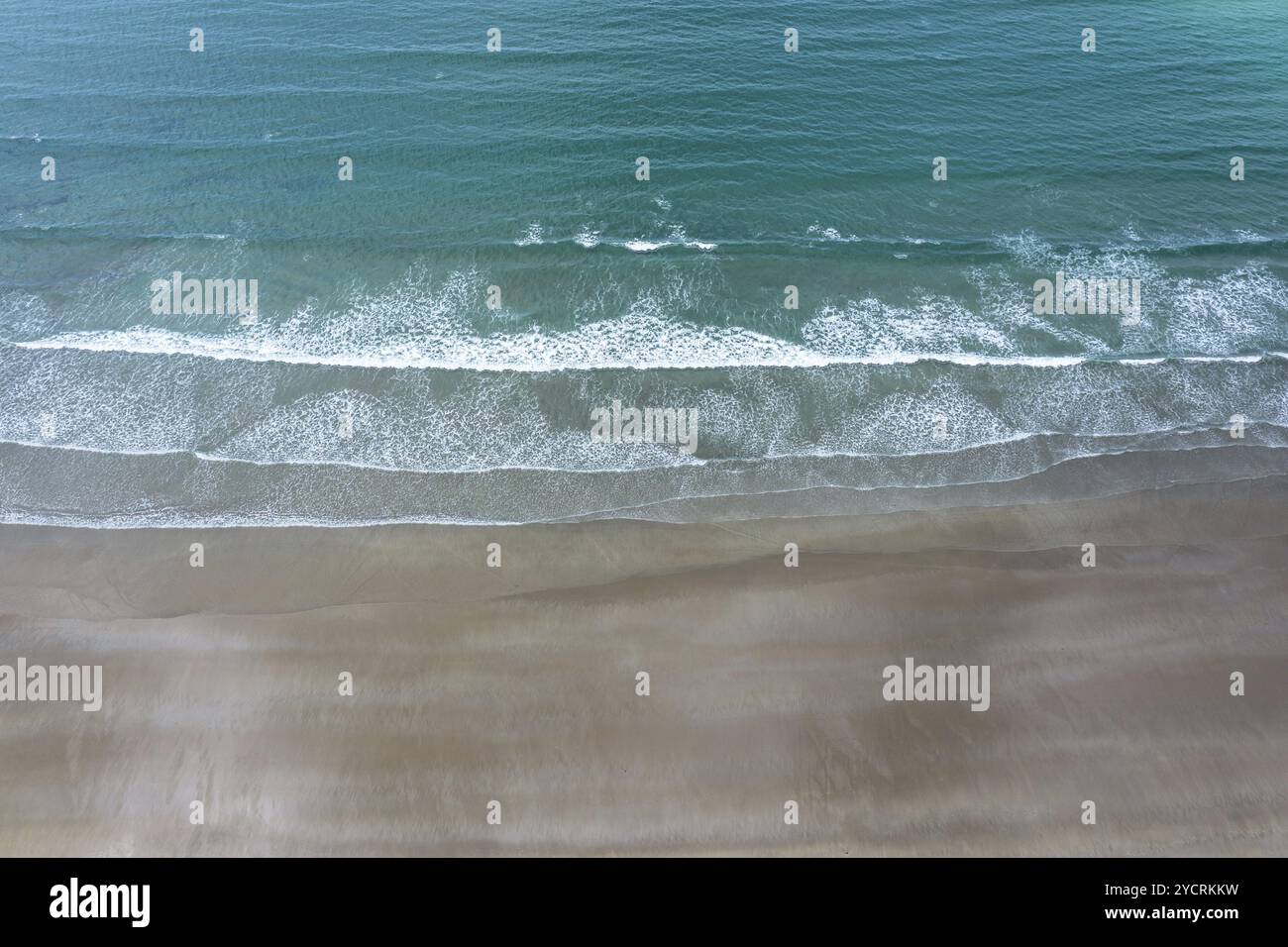 Top-down drone view of turquoise ocean and whitecapped waves breaking on an empty golden sandy beach Stock Photo