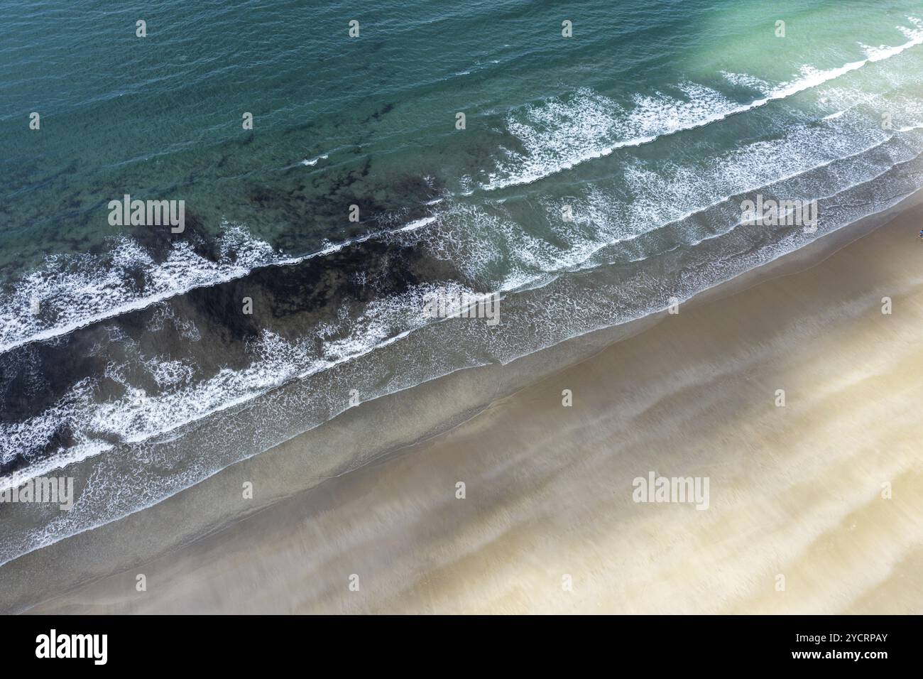 Top-down drone view of turquoise ocean and whitecapped waves breaking on an empty golden sandy beach Stock Photo