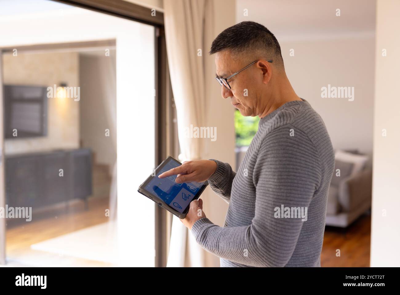 Asian senior man using tablet to control smart home system by window Stock Photo