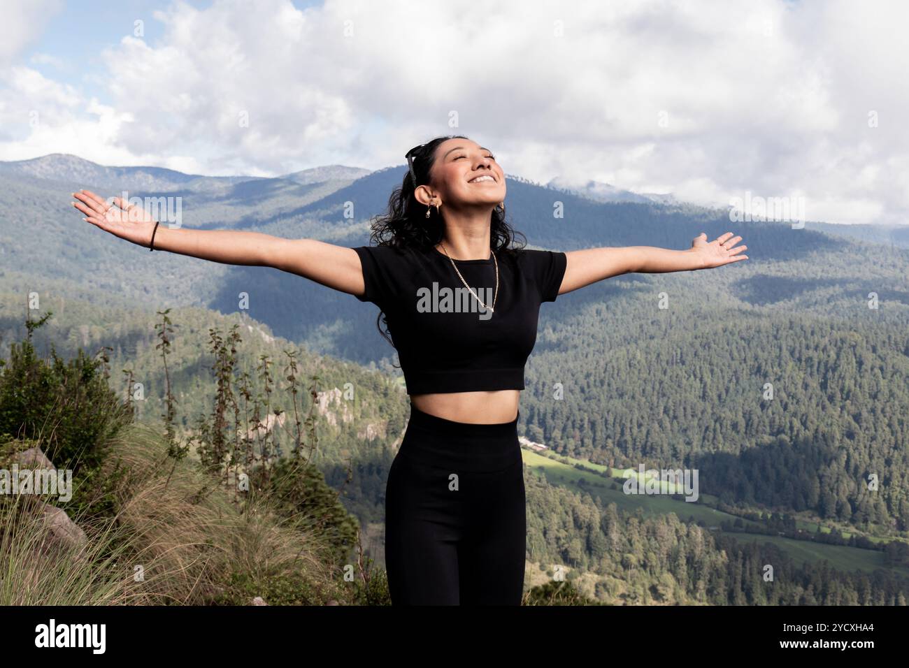 A joyous woman with arms spread wide embraces the picturesque landscape of Cumbres del Ajusco, Mexico City She enjoys a serene moment against a backdr Stock Photo