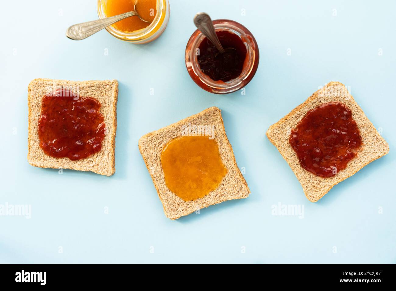 An aerial view of toast slices topped with strawberry and peach jam alongside open jars Stock Photo