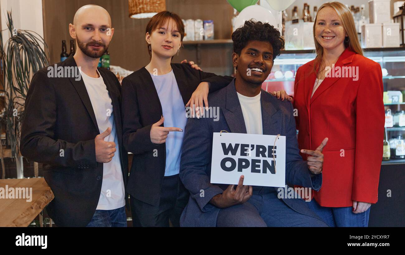 Diverse group of colleagues pose together, holding we are open sign to ...