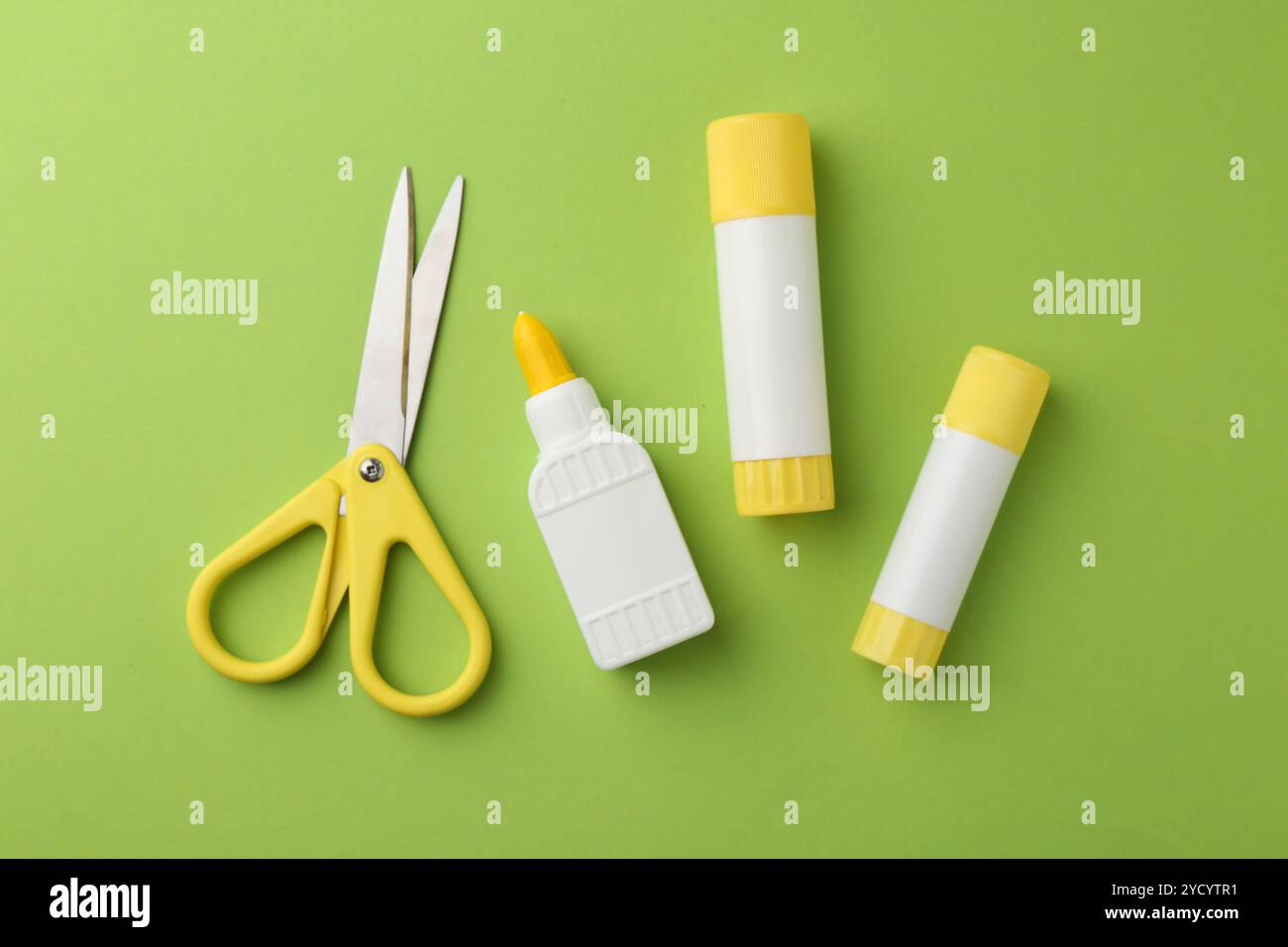Different types of glue and scissors on green background, flat lay ...
