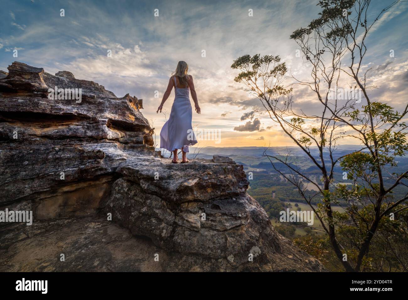Standing on a cliff edge with dress blowing in the wind she dreams ...