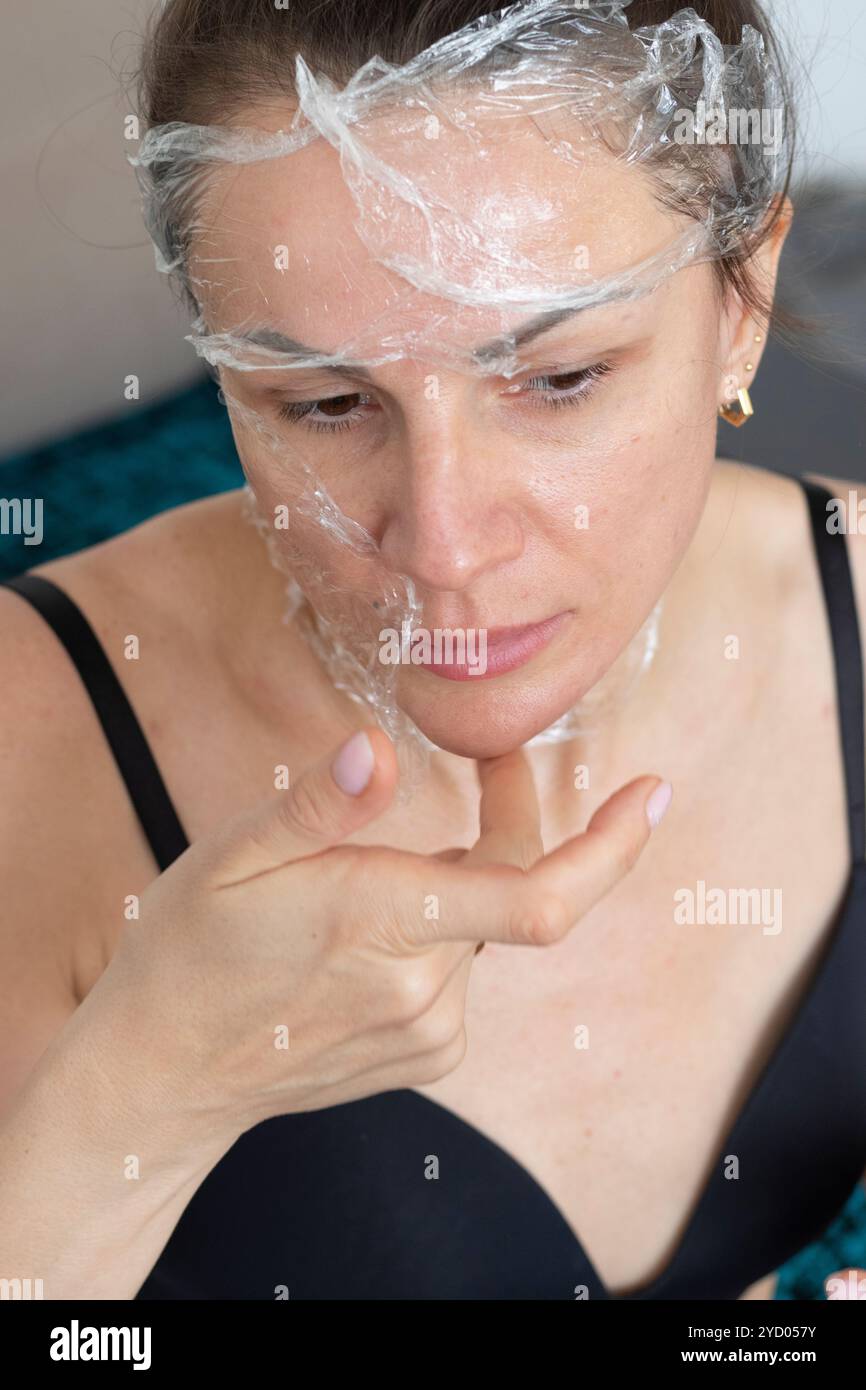 Woman wrapping her face and neck with a cling film wrap as a skin care therapy Stock Photo