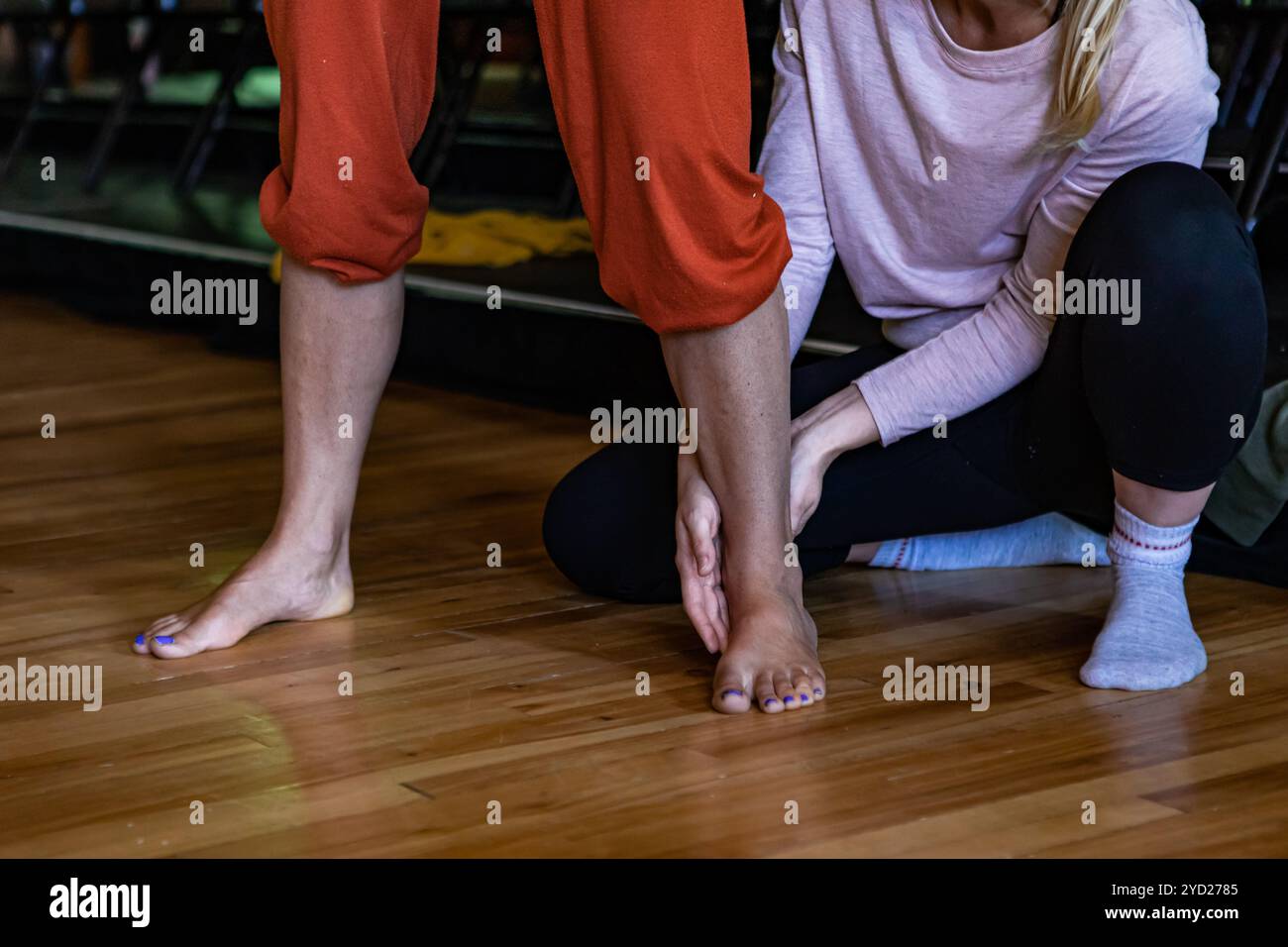 Yoga teacher correcting the feet of her student Stock Photo - Alamy