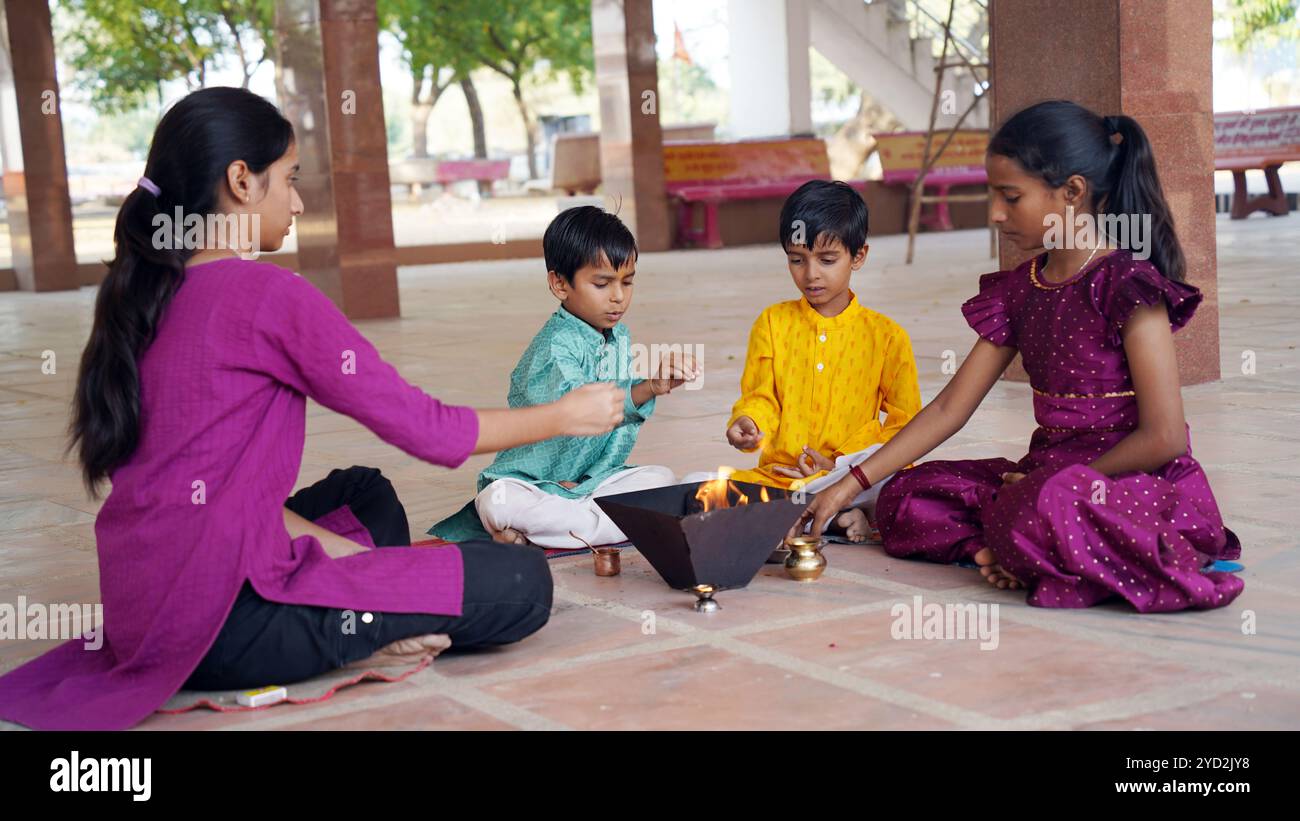 An Indian family in traditional attire performs a Yagya or Havan, led by a priest, to balance energies in their home. This sacred pooja is for harmony Stock Photo