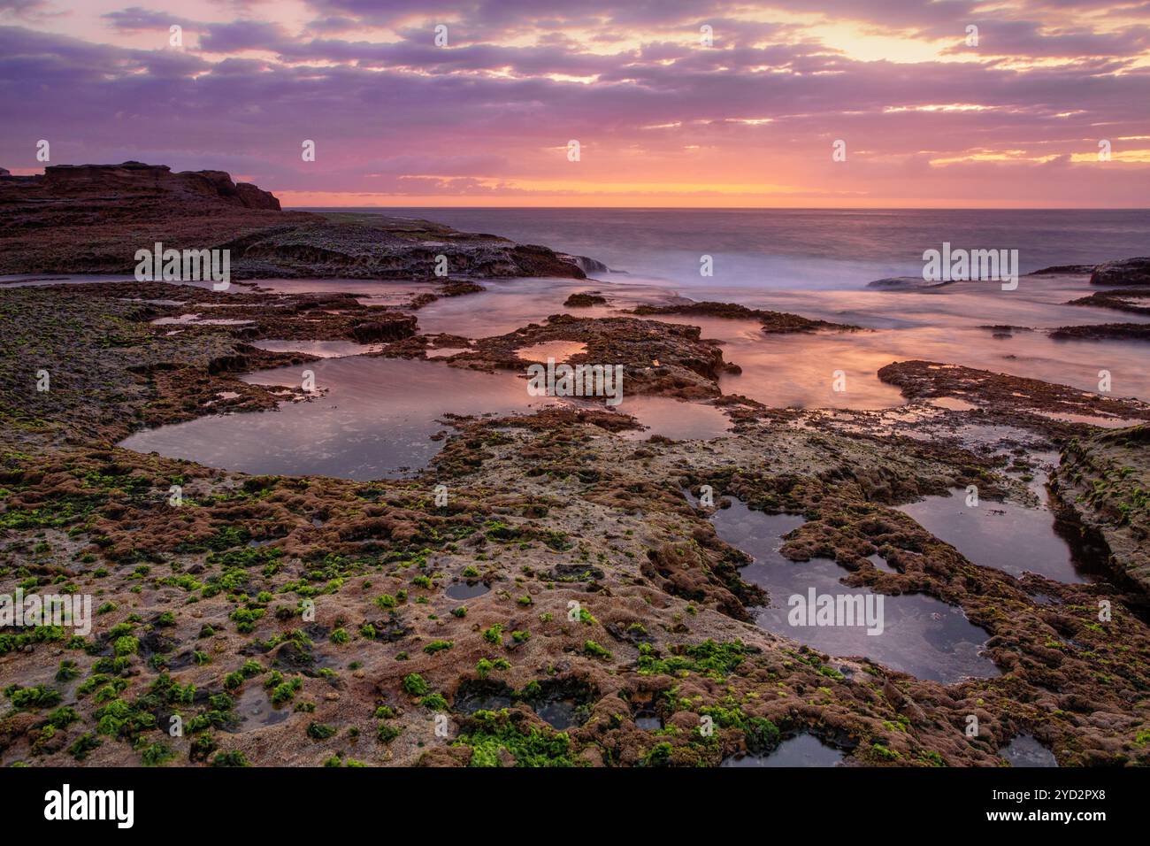 Coastal dawn skies at low tide exposing the rocky reef Stock Photo