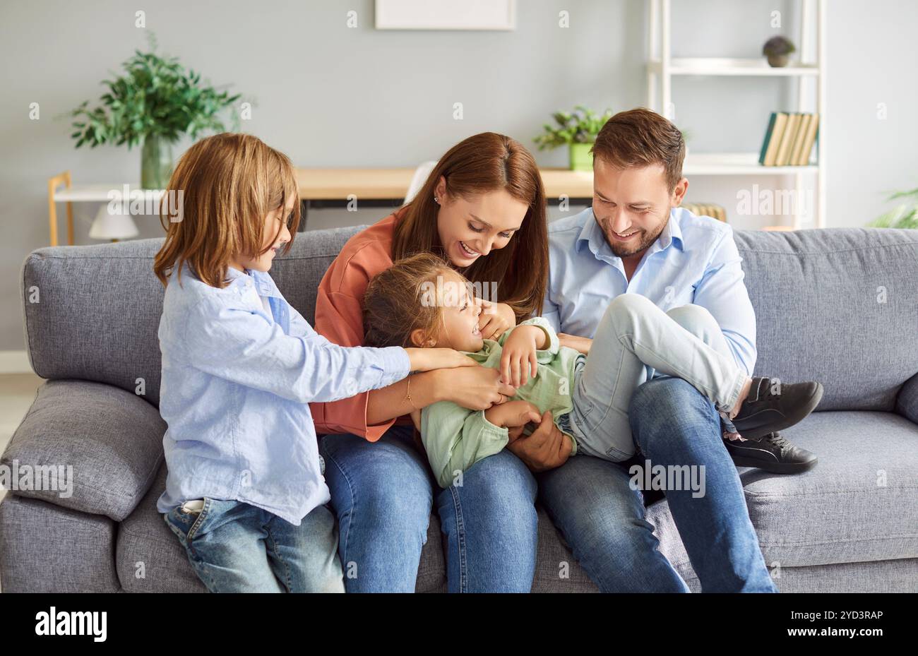 Family fun, cheerful excited parents tickling beloved kid girl, playing with child at home laughing  Stock Photo