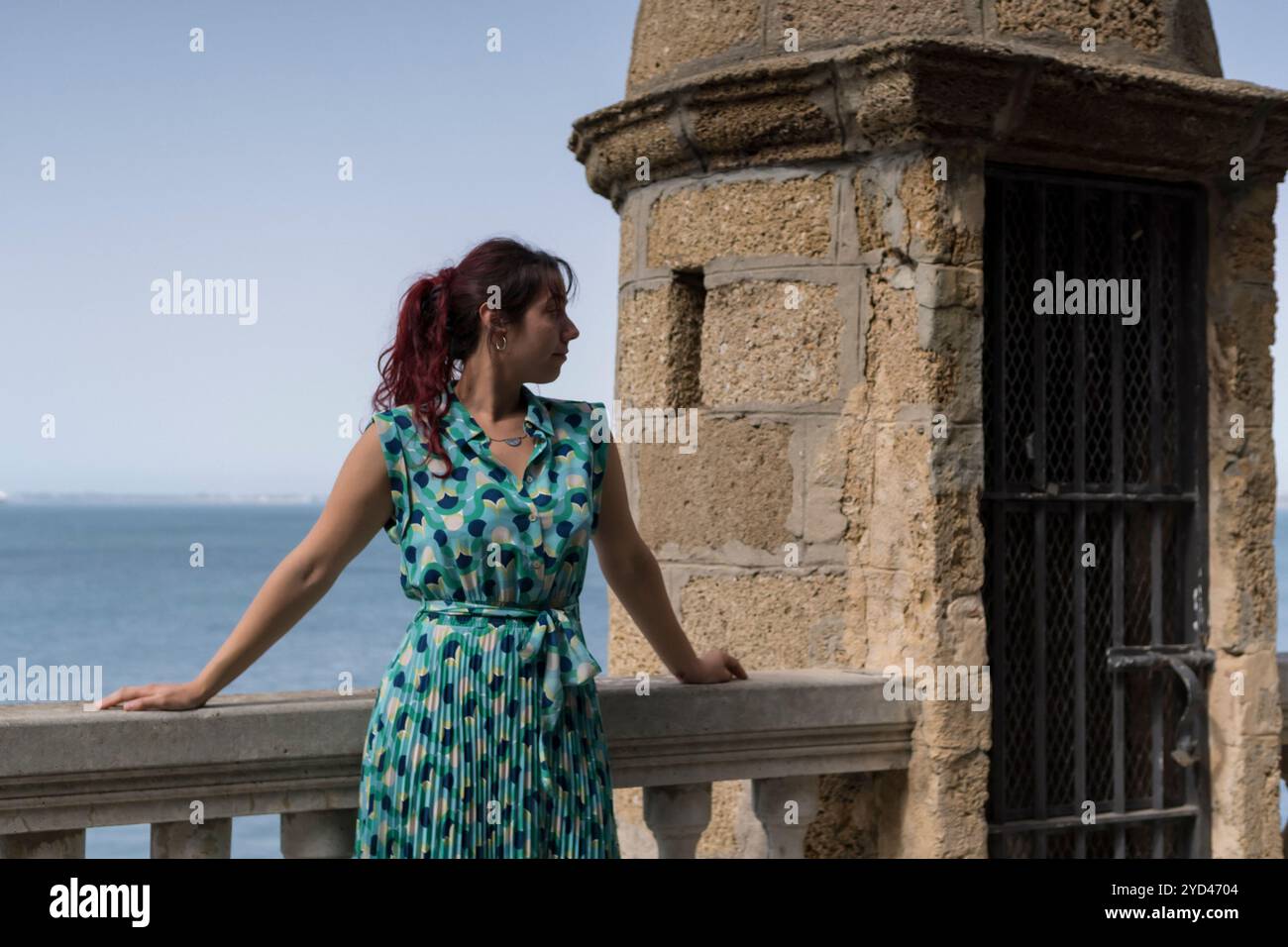 Redhead woman leaning on a railing with the sea in the background Stock Photo