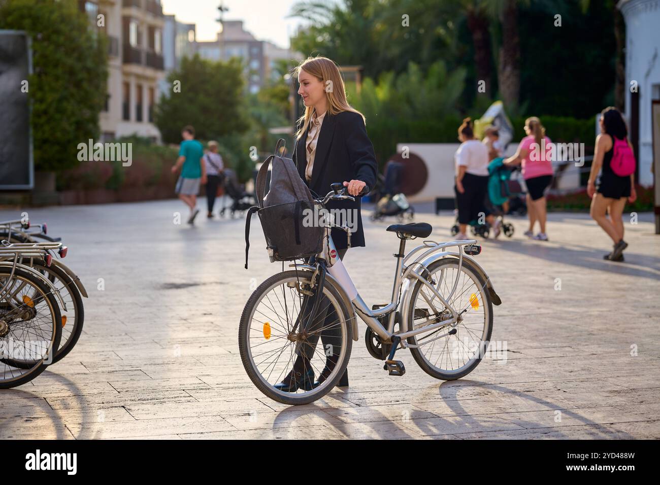 Woman in business attire stands beside a bicycle Stock Photo