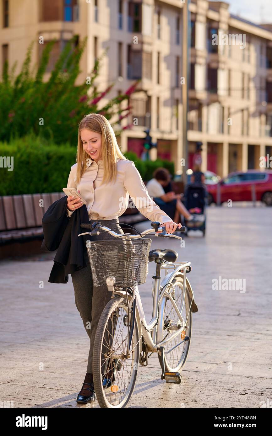 Young woman checking her phone while standing beside a bicycle Stock Photo