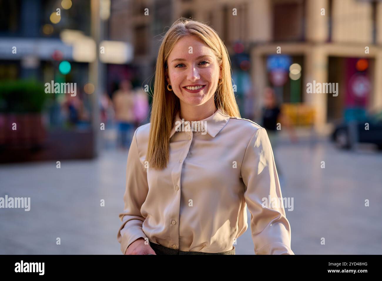 Young woman smiling confidently on a sunny day in an urban city square Stock Photo