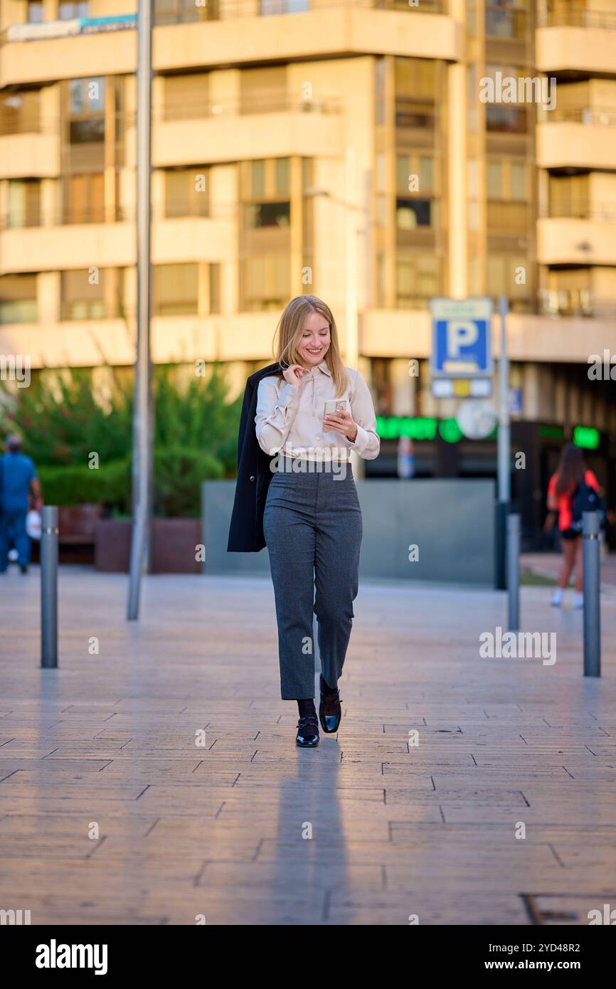 Young woman in business attire checks her phone in a city setting Stock Photo