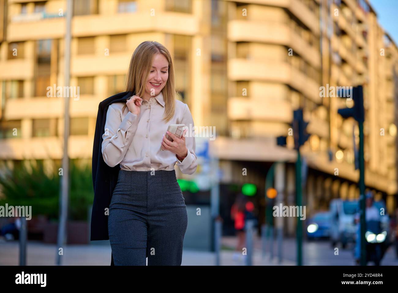 Young woman in business attire checks her phone in a city setting Stock Photo