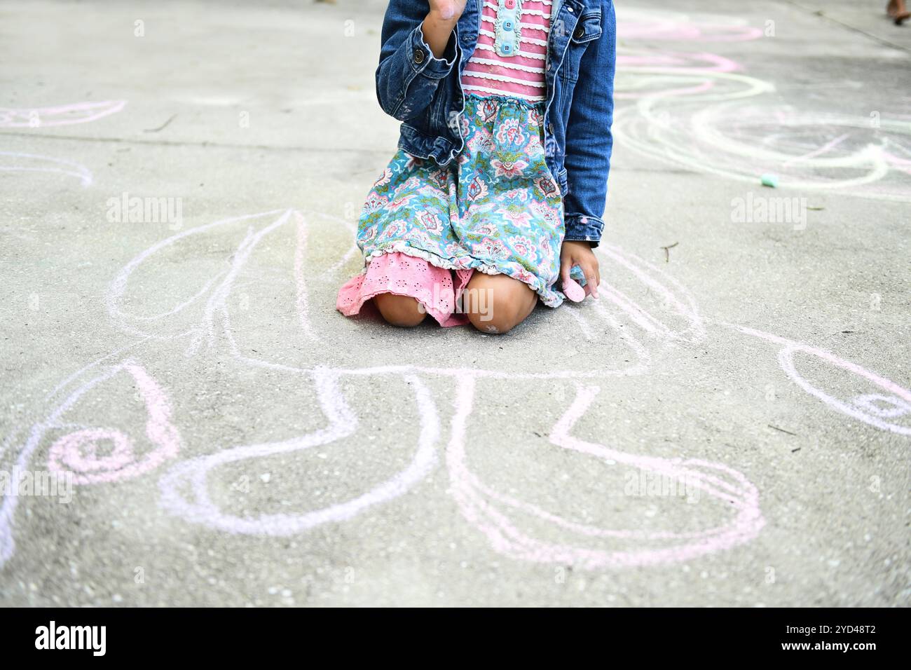 Child kneeling on pavement, holding chalk, large chalk drawing b Stock Photo