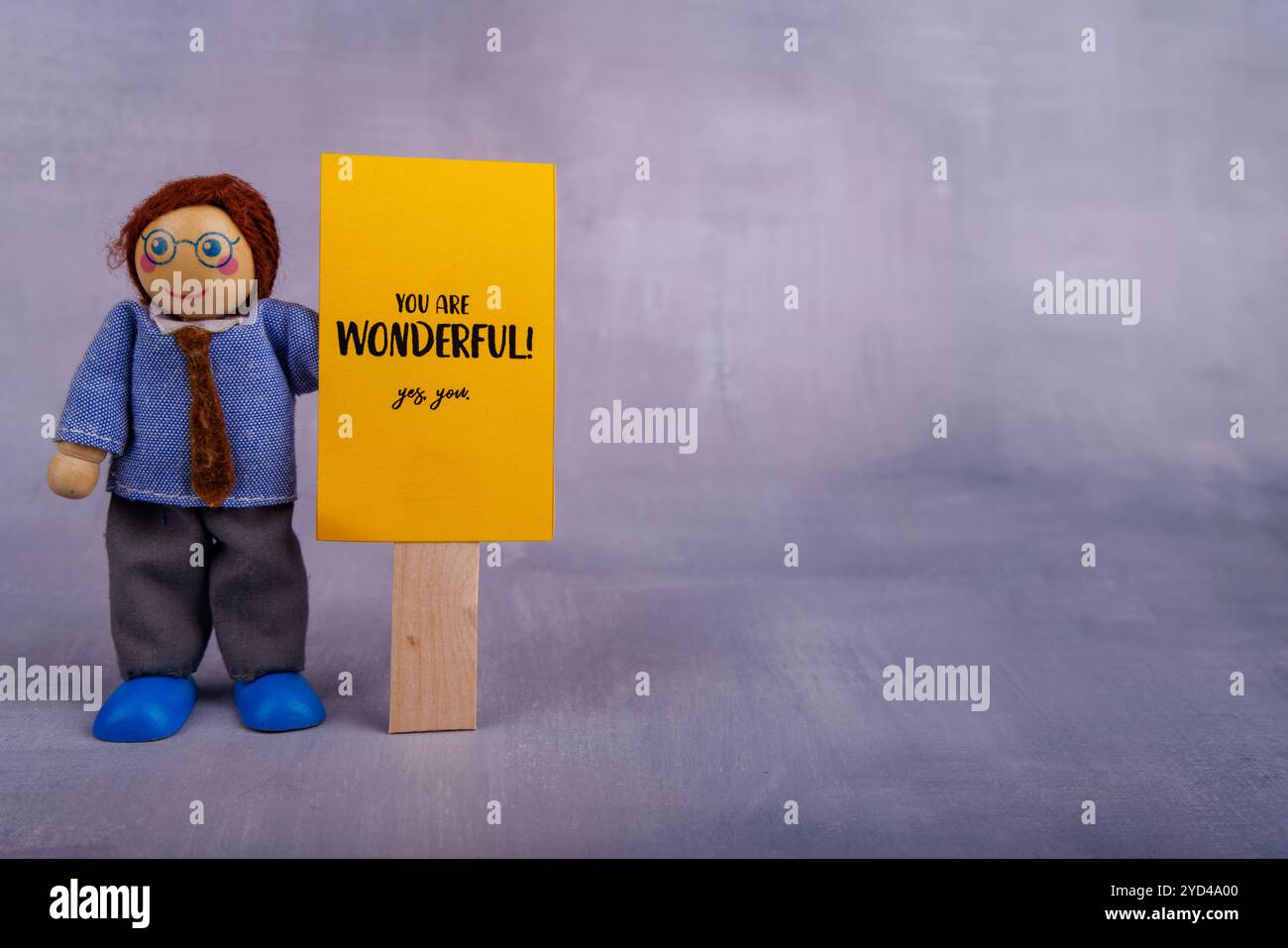 A wooden toy figure holds a yellow sign with a positive message, radiating optimism and motivation through its simple, playful design Stock Photo