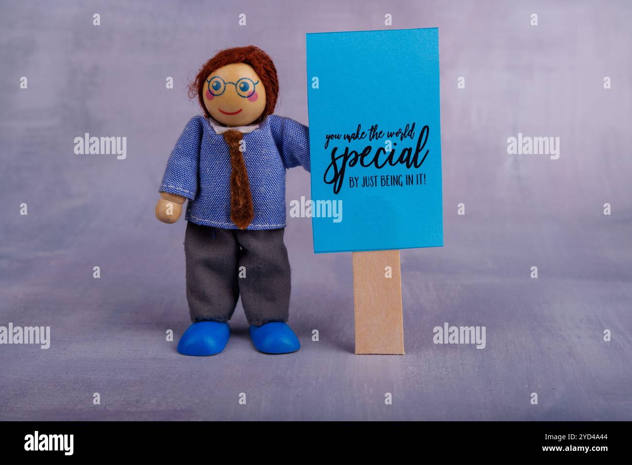 A joyful wooden toy holds a blue motivational banner, representing self-confidence and positivity, set against a vibrant backdrop Stock Photo